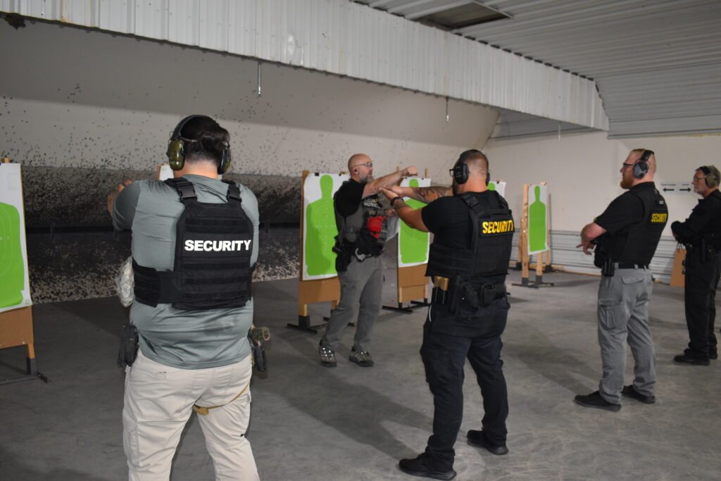 A group of security personnel in tactical vests practicing shooting at training targets indoors. They are engaged in gun training, with green silhouette targets positioned in front of them.
